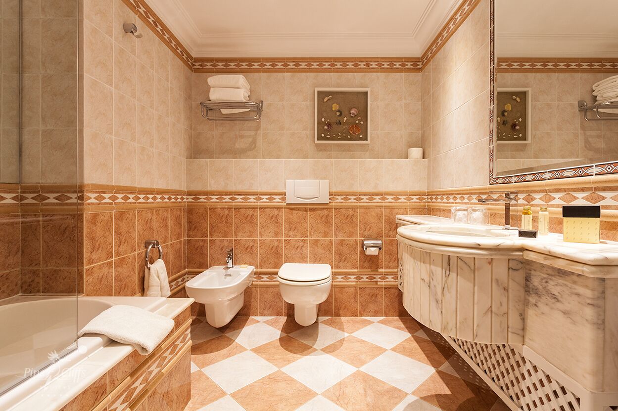 Un baño con bañera, dos inodoros, un bidé y un lavabo con espejo.