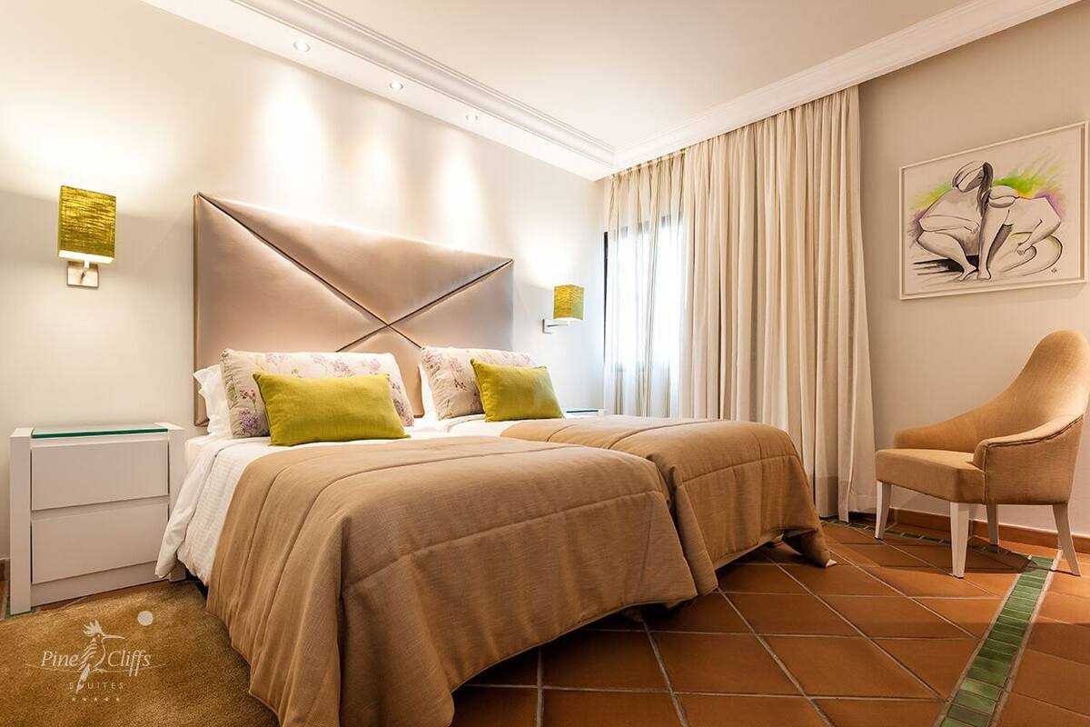 A hotel room with a bed, two pillows, a chair, and a painting on the wall.