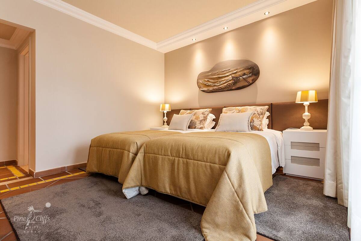 A hotel room with a large bed, two bedside tables with lamps, a decorative wall piece, and a grey carpet.