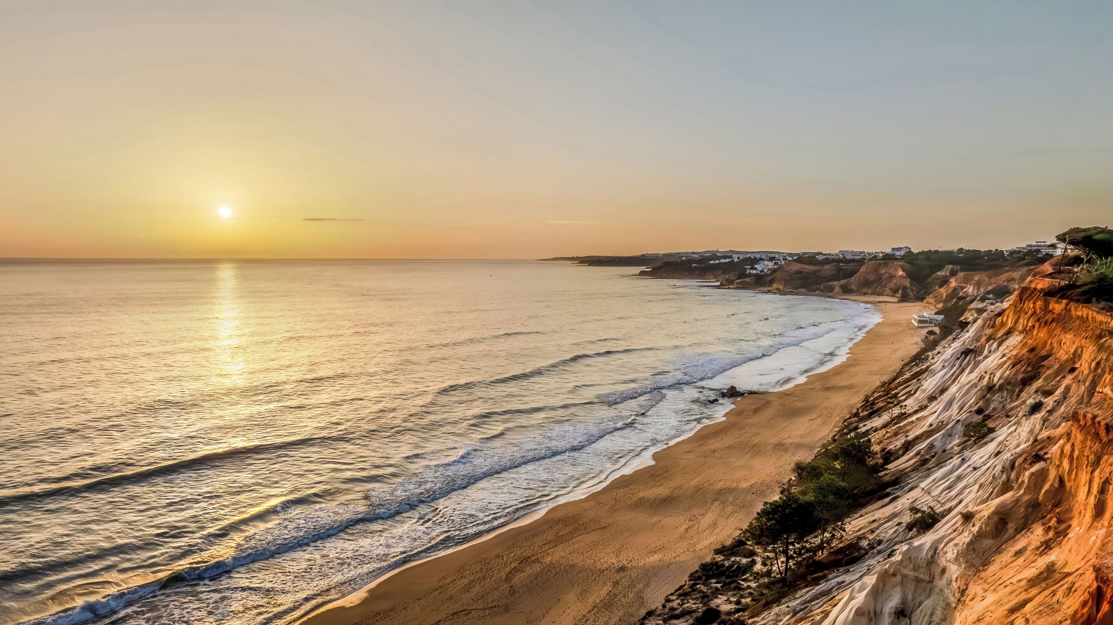 Un paysage côtier avec une plage de sable, de douces vagues et une falaise.