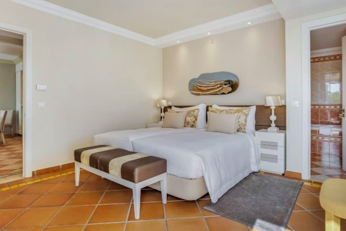 A bedroom with a double bed, a bedside table, a bench, and a rug.