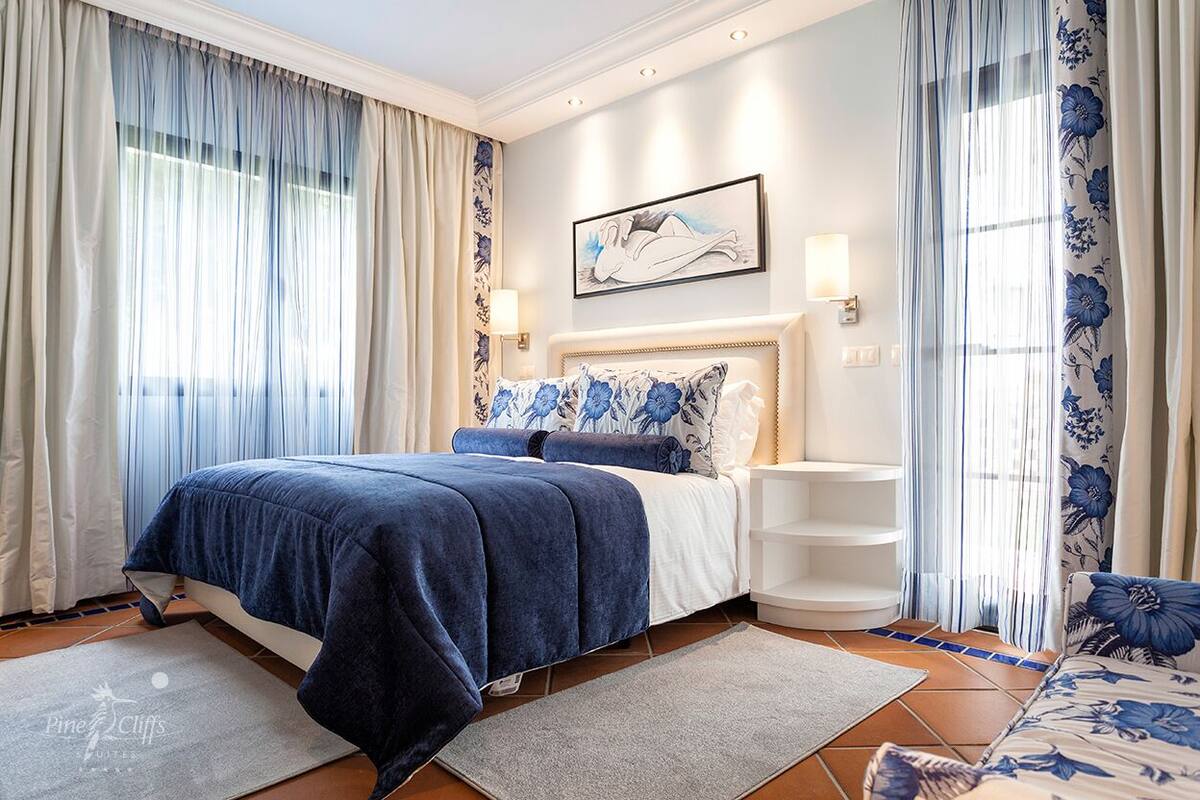 A bedroom with a large bed, a bedside table, a wall-mounted artwork, and a window with curtains.