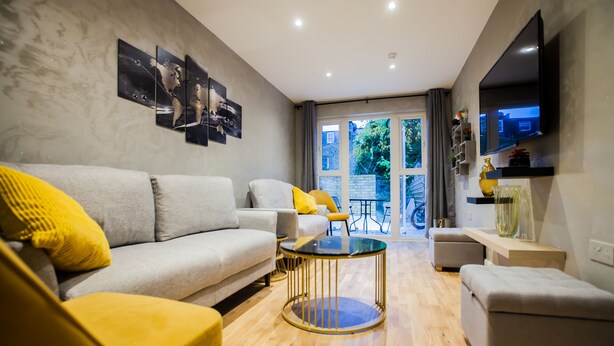 Ein modernes Wohnzimmer mit einem grauen Sofa, gelben Kissen, einem runden Couchtisch und einem an der Wand befestigten Fernseher.