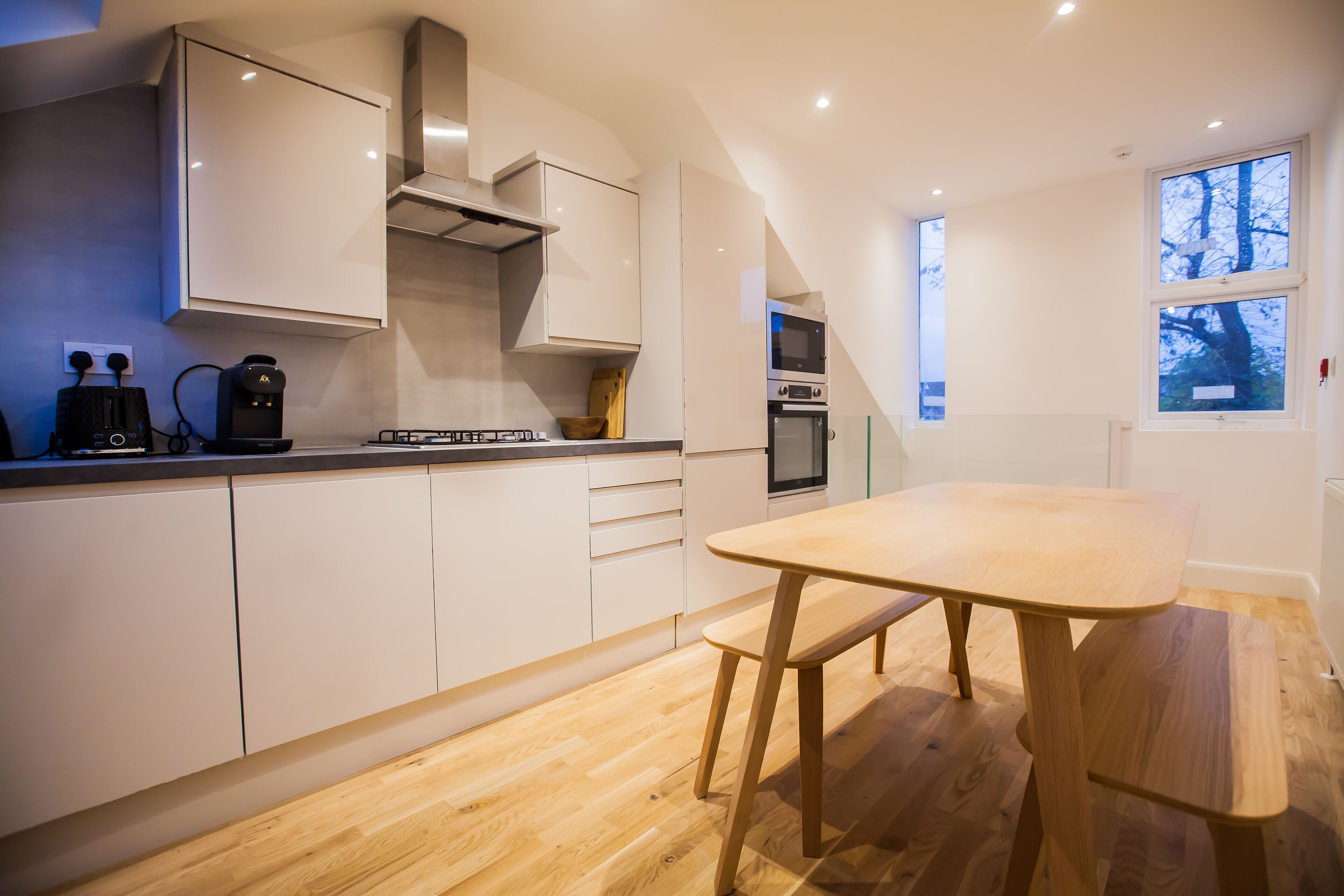 A modern kitchen with white cabinets, a wooden table, and a built-in oven.