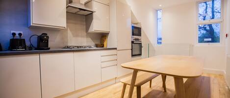 A modern kitchen with white cabinets, a wooden table, and a built-in oven.