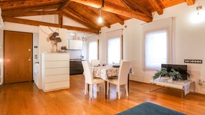 Een ruime woonkamer met een houten plafond, een eettafel met stoelen, een keuken op de achtergrond en een televisie op een standaard.