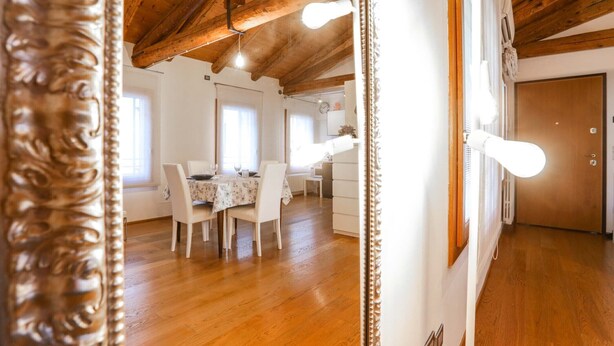 Een eetruimte met een houten plafond, een tafel met stoelen en een witte wand met een lamp.