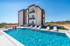 Um edifício moderno com piscina, várias varandas e um céu azul límpido.