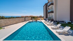A swimming pool with lounge chairs, a view of the sea, and a building with balconies. - Deluxe Villa Laura with Pool Studio 4b (Novalja)