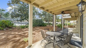 A covered patio with a table and chairs, surrounded by plants and trees.