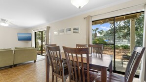 A dining area with a large table and chairs, a sofa, and a view through glass doors to an outdoor patio.