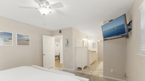 A bedroom with a bed, a ceiling fan, a TV mounted on the wall, and a bathroom visible through an open door.