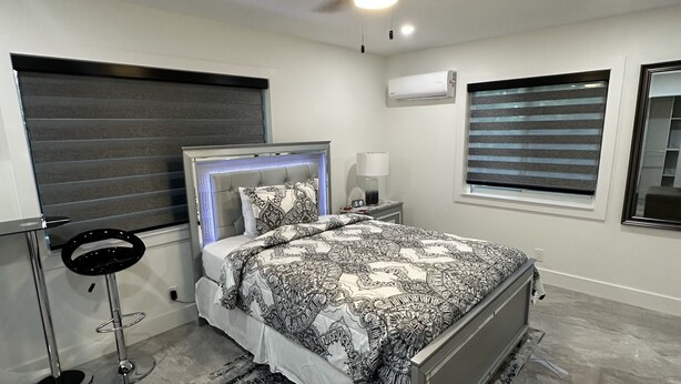 Un dormitorio moderno con cama, ventilador de techo, aire acondicionado y ventana con persianas.