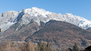 Un paysage montagneux, avec des sommets enneigés et une vallée parsemée d’arbres et de bâtiments.