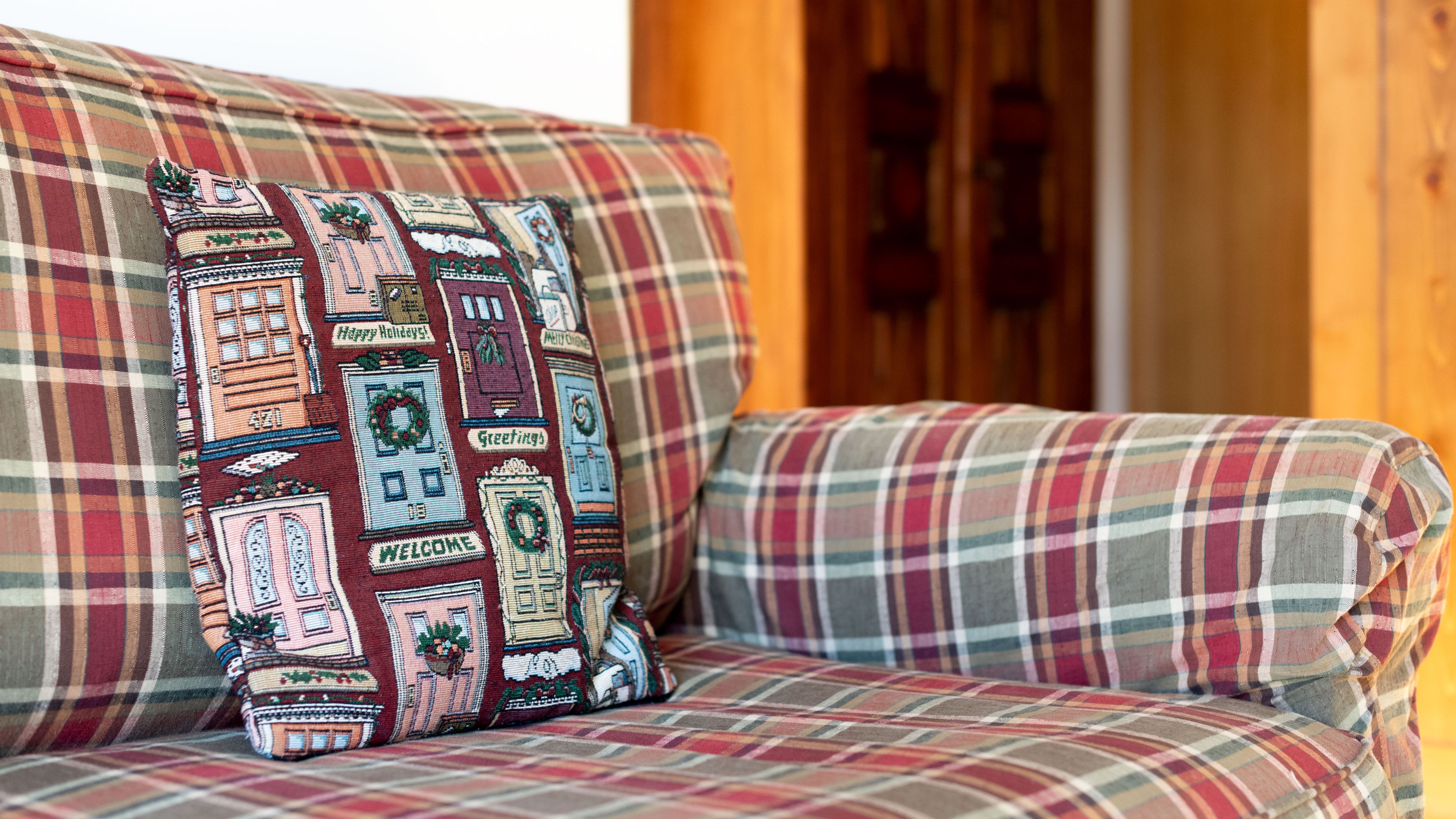 A plaid sofa with a decorative pillow featuring holiday-themed patches.