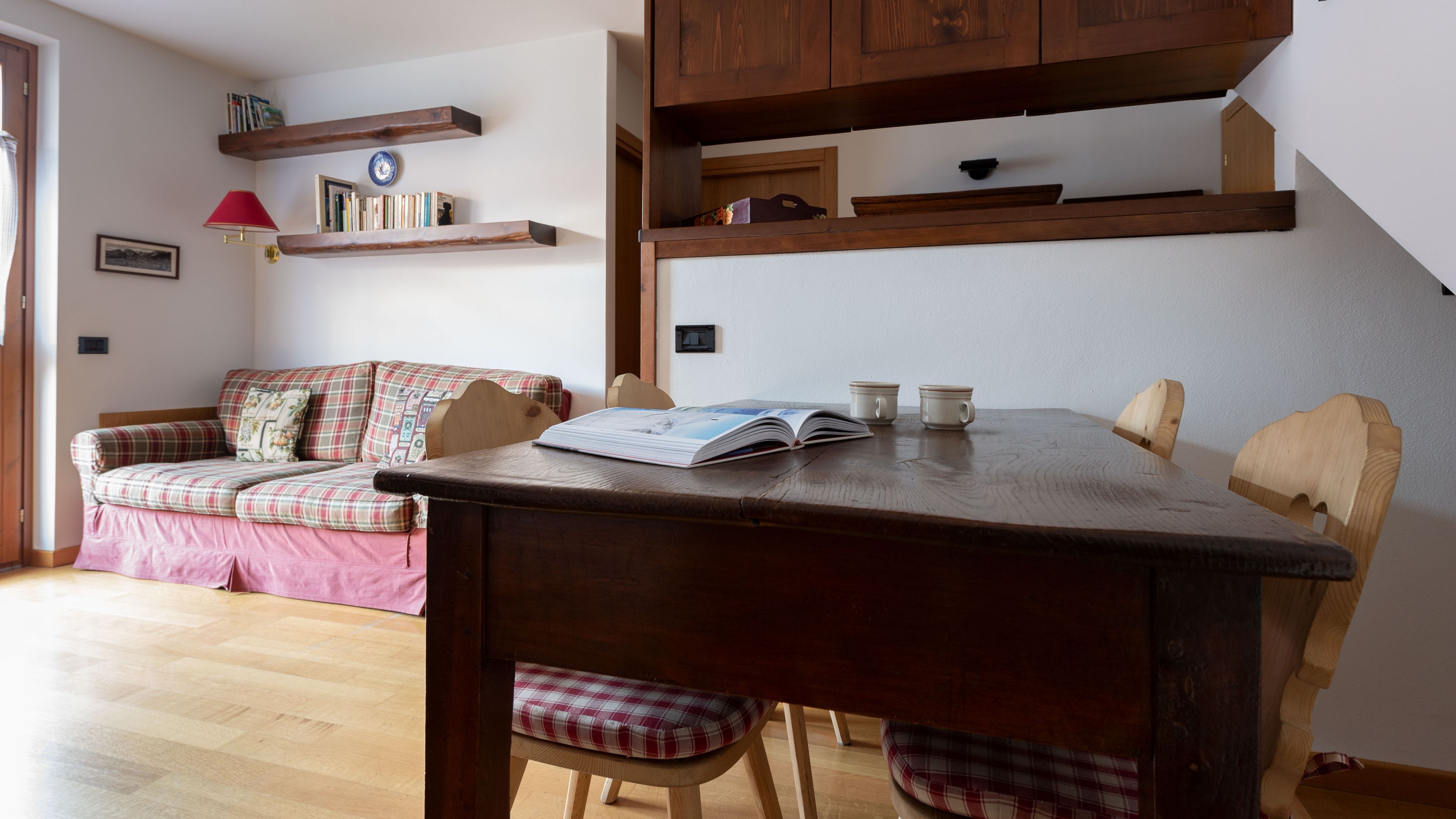 Un salón acogedor con una mesa de madera, un sofá escocés y una estantería.