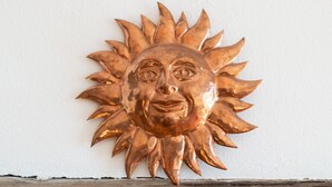 Un élément décoratif mural en bronze, en forme de soleil et orné d’un visage.