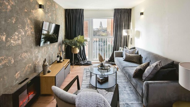 Ein modernes Wohnzimmer mit grauem Sofa, Couchtisch, Wandfernseher und Kamin.