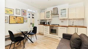 Une cuisine moderne avec des meubles blancs, une cuisinière à gaz et un coin repas comprenant une table en verre et des chaises noires.