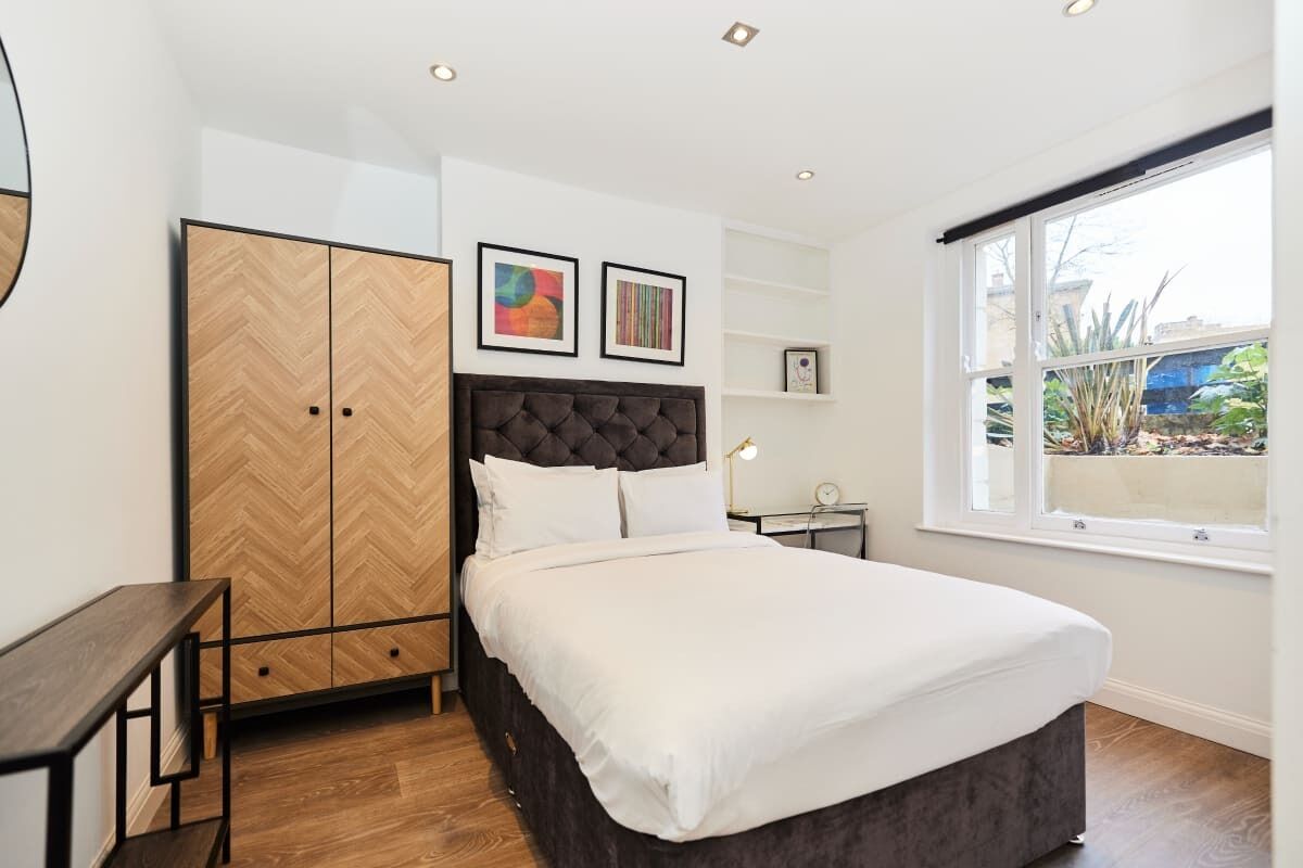 A bedroom with a bed, a wardrobe, a desk, and a window with a view.