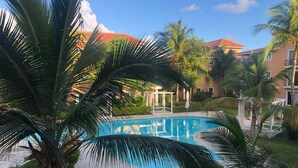 A swimming pool surrounded by palm trees and a building with a red roof. - Beautiful 2-bed Apartment in Punta Cana (Punta Cana)