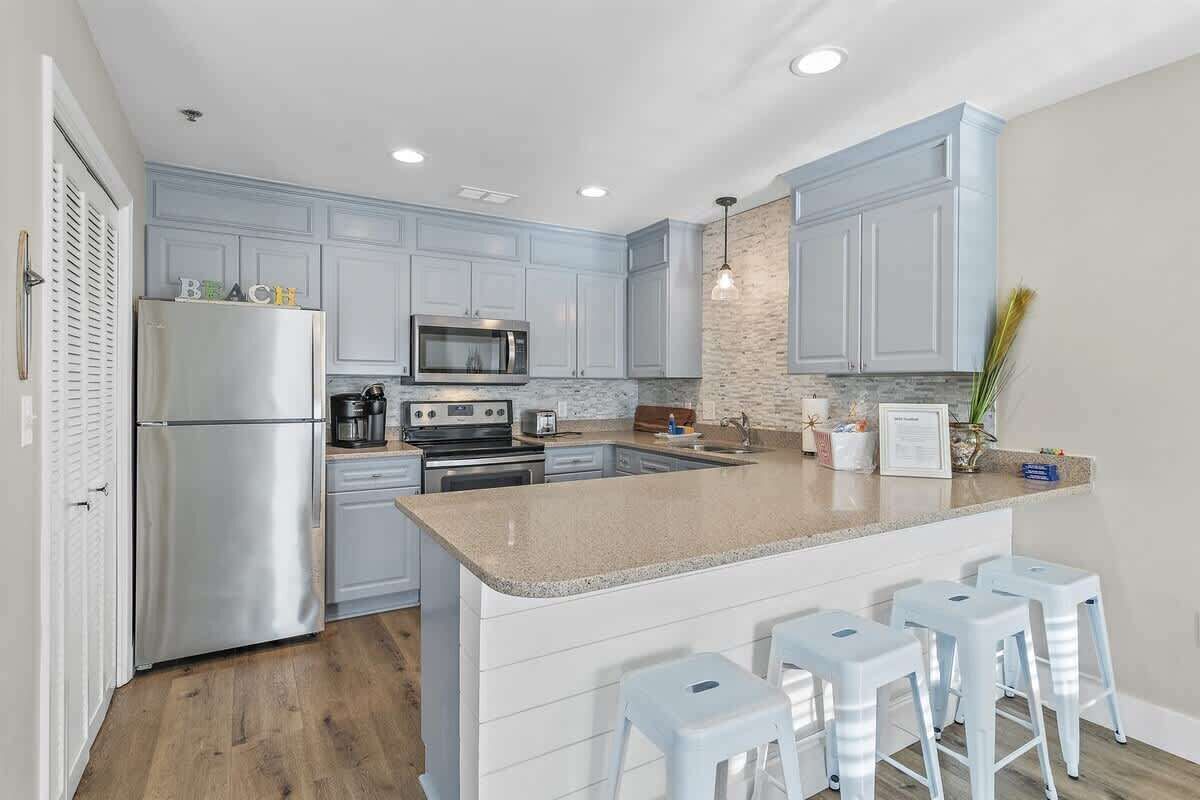 A kitchen with light blue cabinets, stainless steel appliances, a granite countertop, and bar stools.