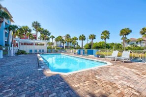 A swimming pool with lounge chairs, palm trees, and a brick patio.