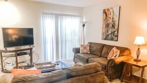 A living room with a sofa, a coffee table, a TV, and a lamp. - Walk to Shands & VA Hospital, UF, Pool Access (Gainesville)