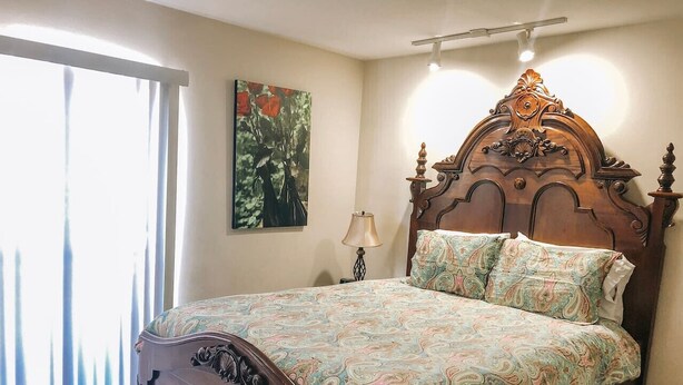 A bedroom with a wooden bed, a nightstand, a lamp, and a painting on the wall. - Walk to Shands & VA Hospital, UF, Pool Access (Gainesville)