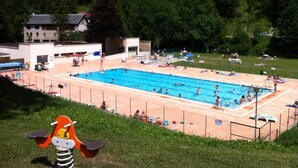 Una piscina rodeada de una zona vallada con una colina cubierta de césped al fondo.