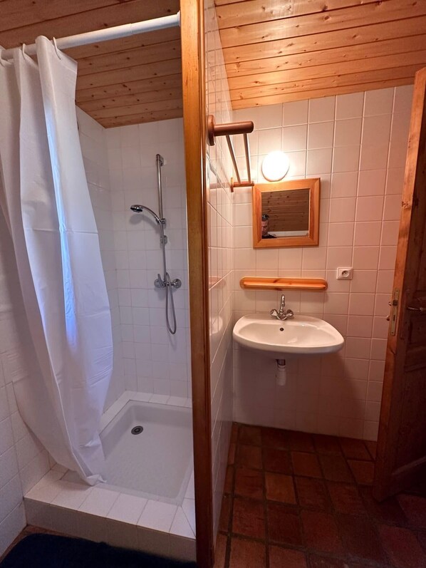 A bathroom with a shower, a sink, and a wooden ceiling.