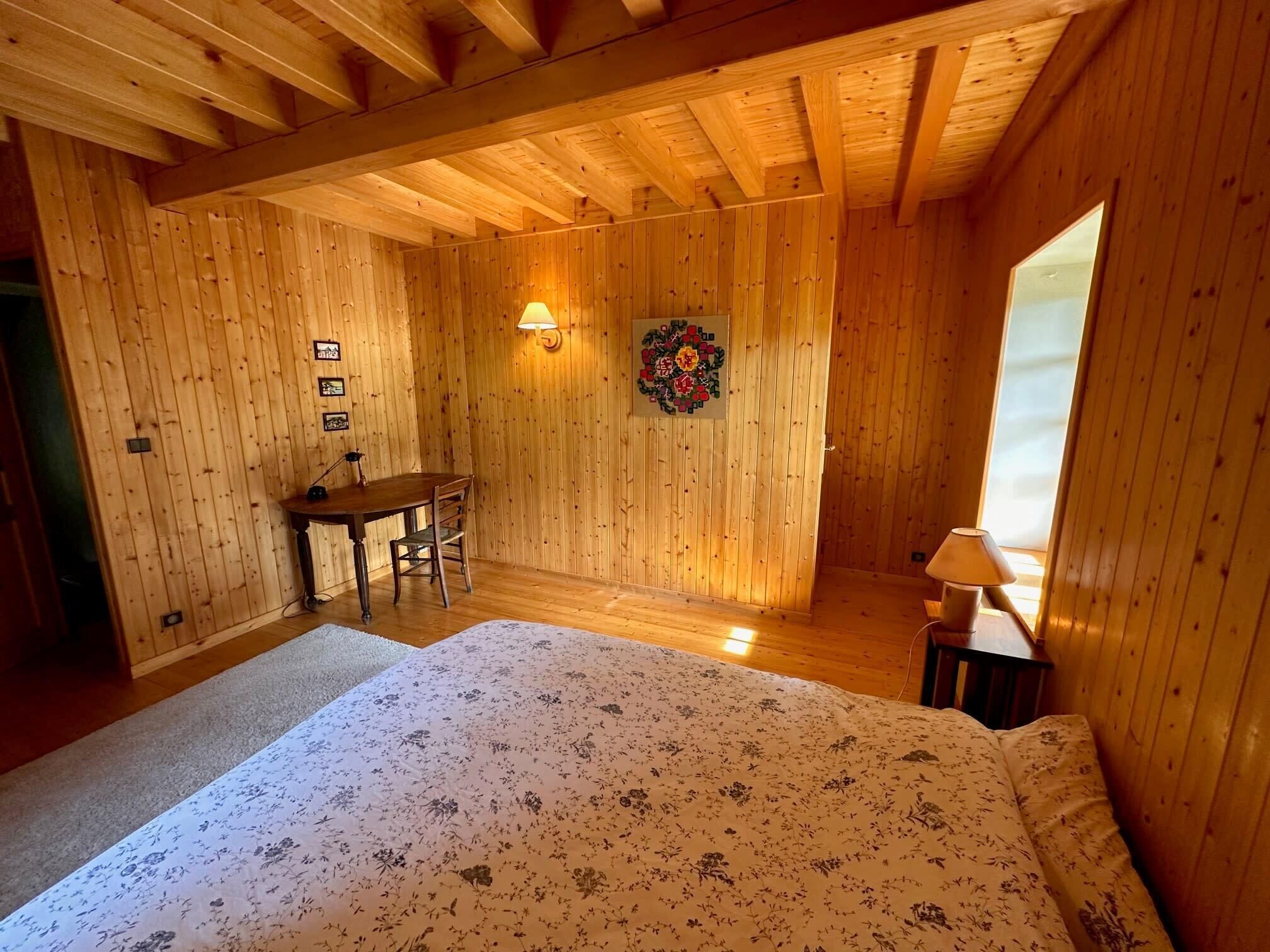 Ein Zimmer in einer Holzhütte mit einem Bett, einem Schreibtisch und einer Lampe.