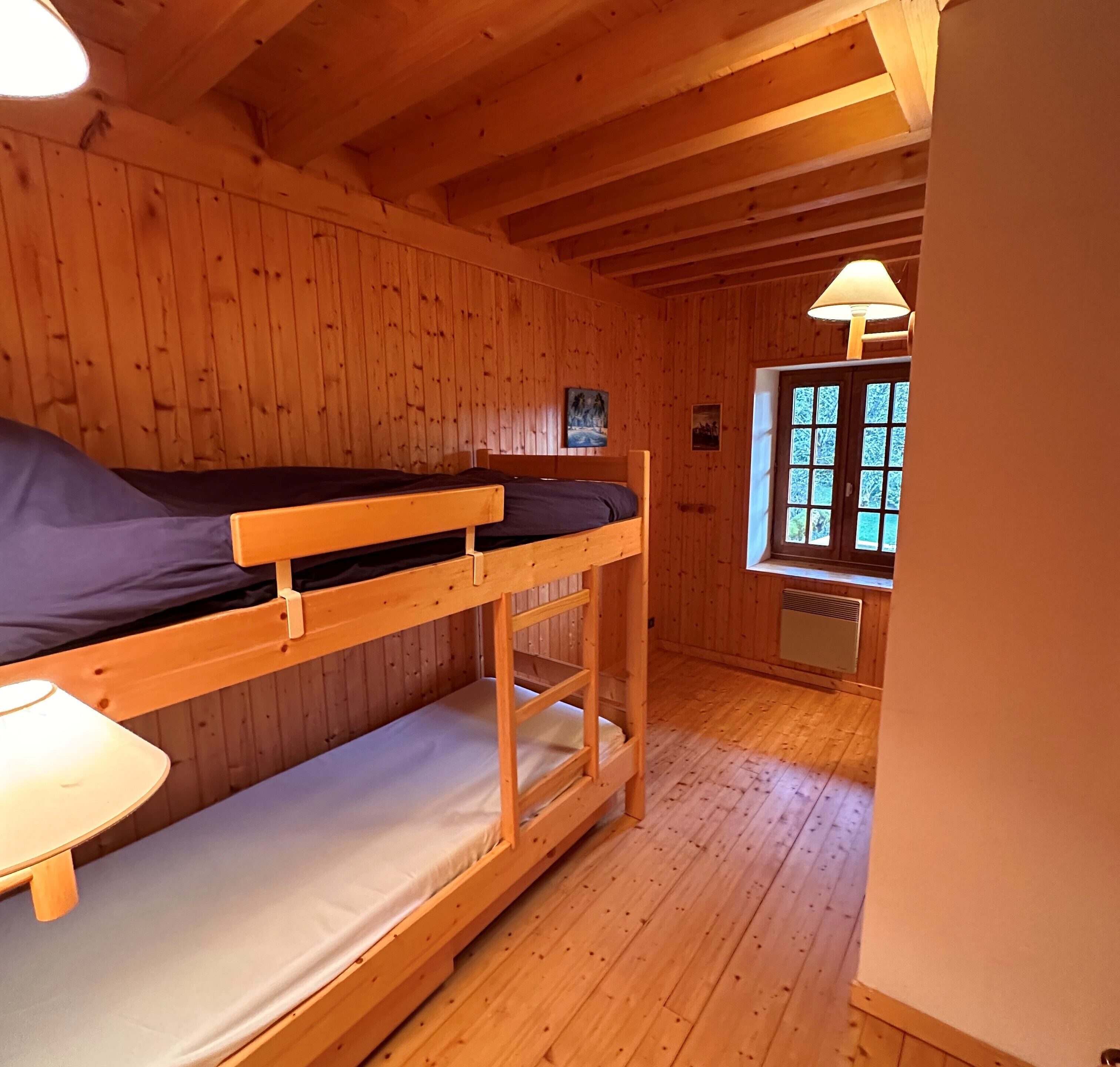 Ein Zimmer in einer Holzhütte mit Etagenbetten, einem Fenster mit Aussicht und einer Lampe.
