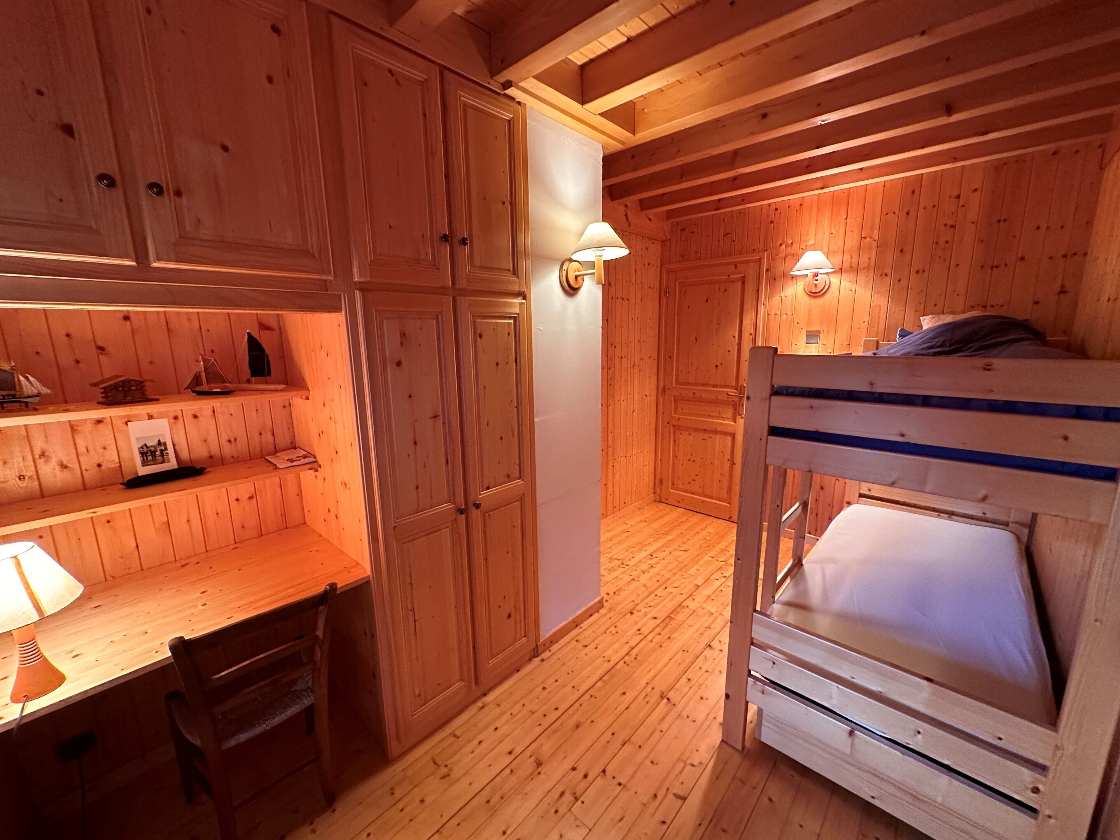 Una habitación de cabaña de madera con literas, un escritorio y una silla, y lámparas fijadas a la pared.