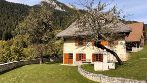 Una casa de piedra con techo inclinado, contraventanas de madera y un muro de piedra que rodea la propiedad.