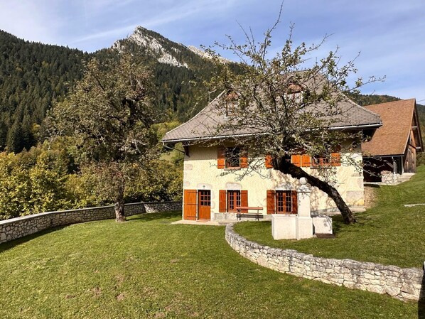 A stone house with a sloped roof, wooden shutters, and a stone wall surrounding the property.