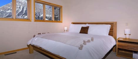 Ein Schlafzimmer mit einem Bett, zwei Nachttischen, einem Fenster mit Blick auf die Berge.