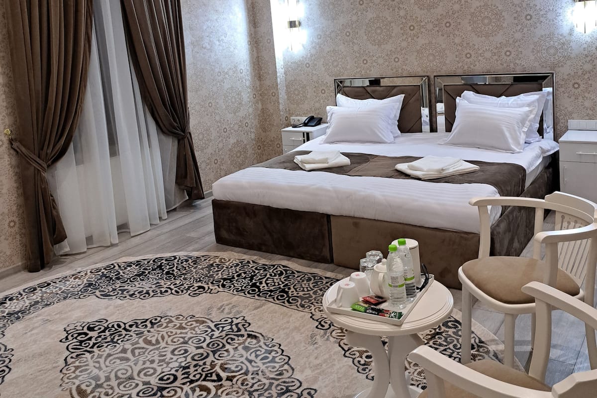 A hotel room with a large bed, a round coffee table, a chair, and a patterned rug.