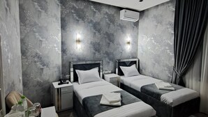 Habitación de hotel moderna con dos camas, un escritorio y una silla. Incluye luces fijadas en la pared y un equipo de aire acondicionado.