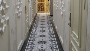 Un pasillo con alfombra estampada, paredes blancas y puertas con lámparas.