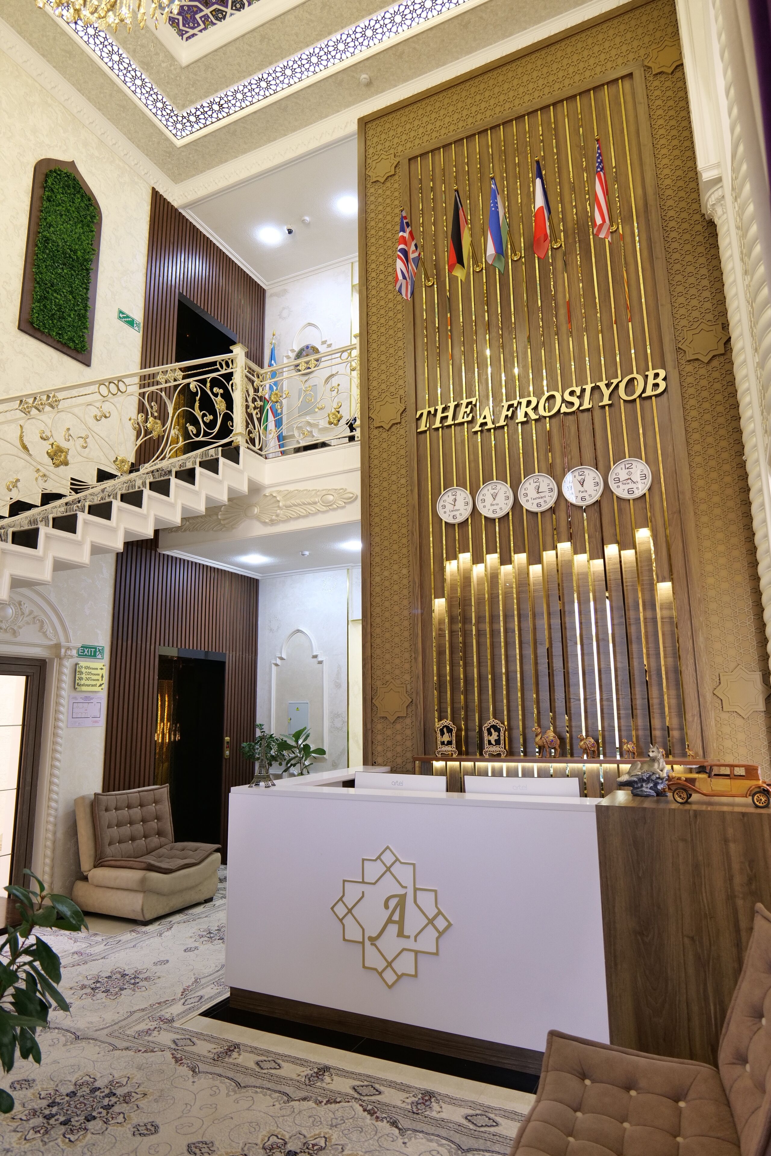 A reception area with a high ceiling, a staircase, and a wall with flags and clocks.