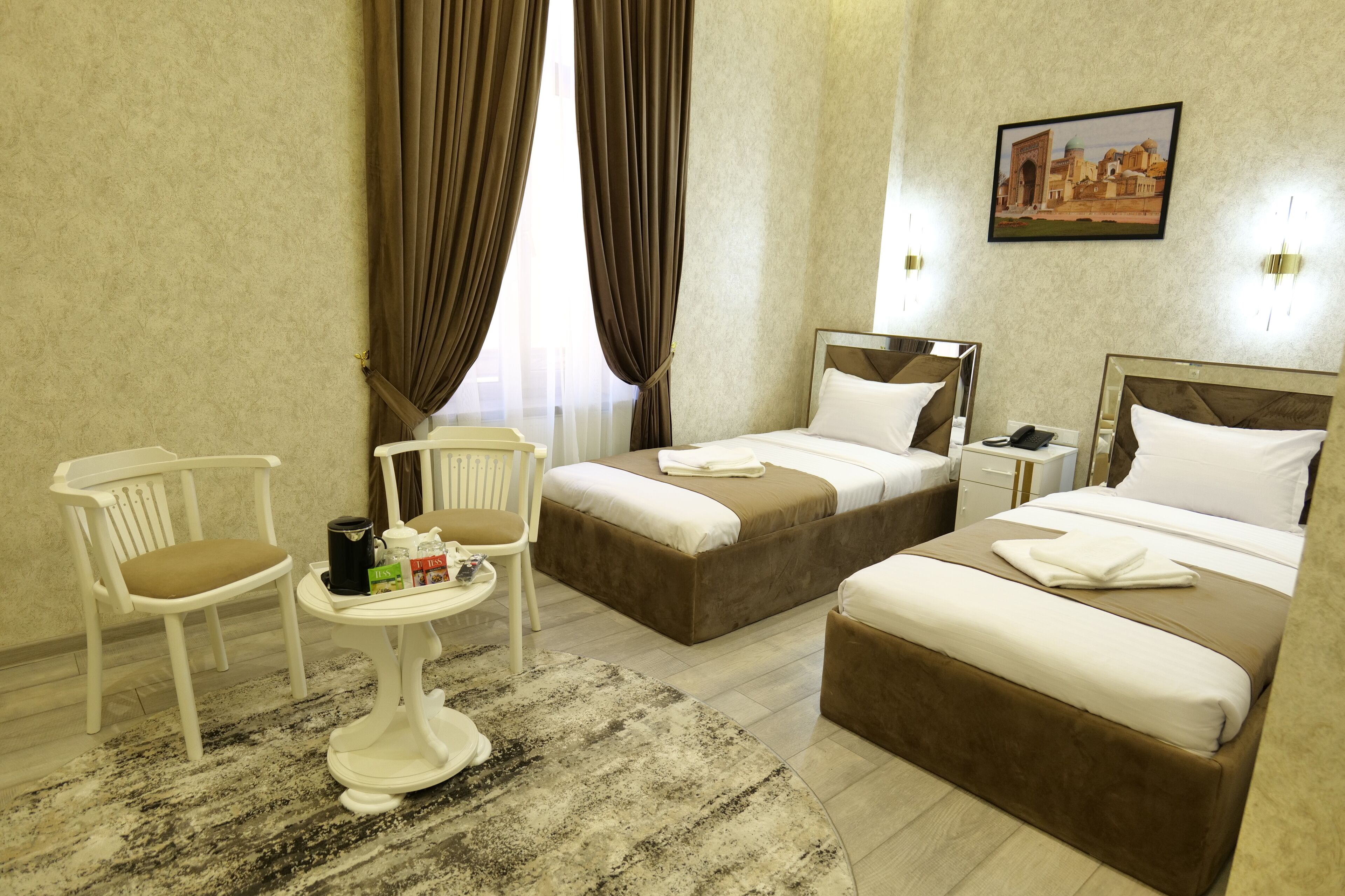 Une chambre d’hôtel avec deux lits, une petite table avec une chaise et une grande fenêtre avec des rideaux.