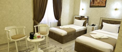 Une chambre d’hôtel avec deux lits, une petite table avec une chaise et une grande fenêtre avec des rideaux.