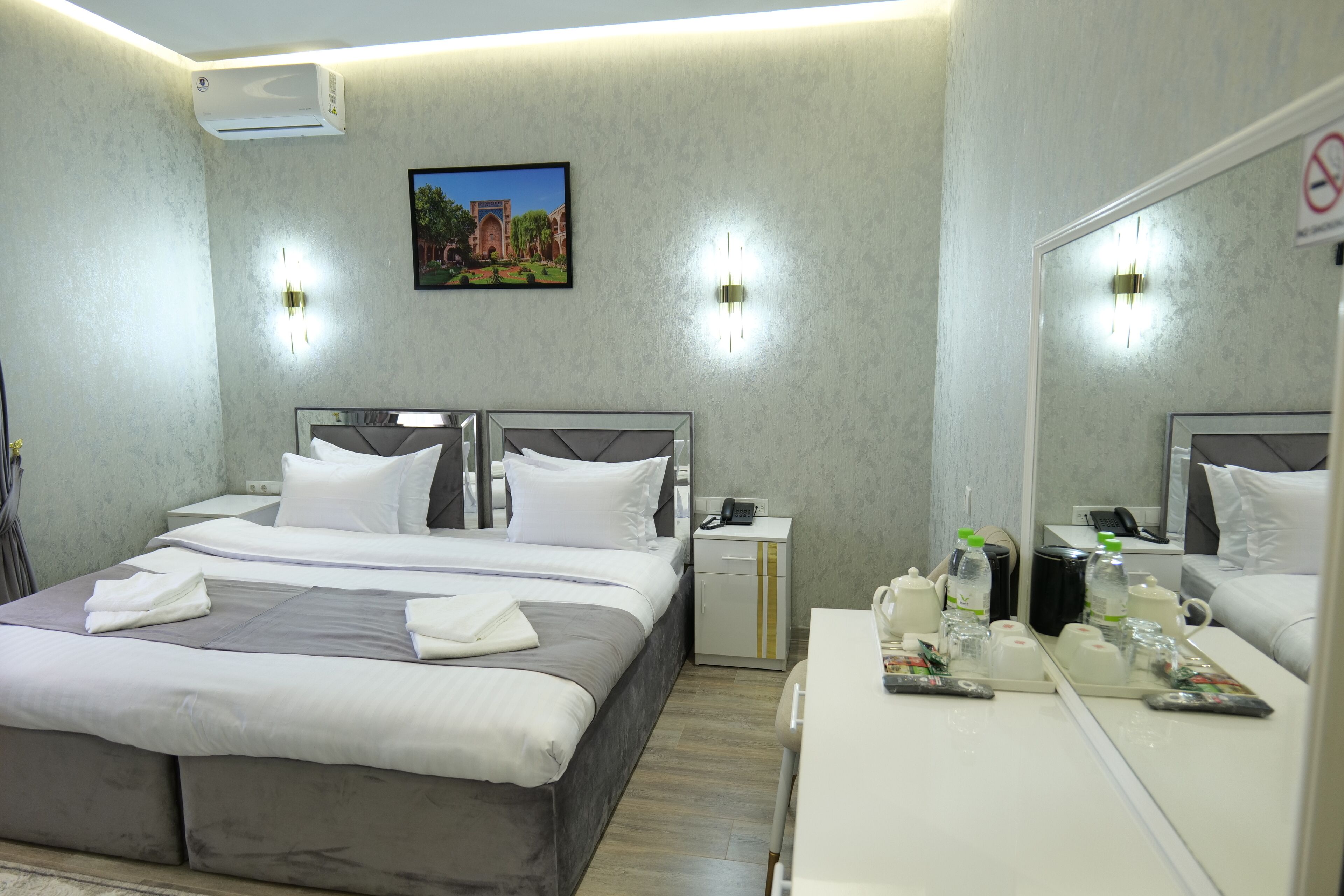 A modern hotel room with a large bed, bedside tables, a mirror, and a small desk with toiletries.