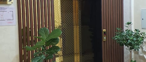 Zona de recepción de un hotel con un separador de madera, una planta en maceta, un extintor y una puerta con cerradura electrónica.