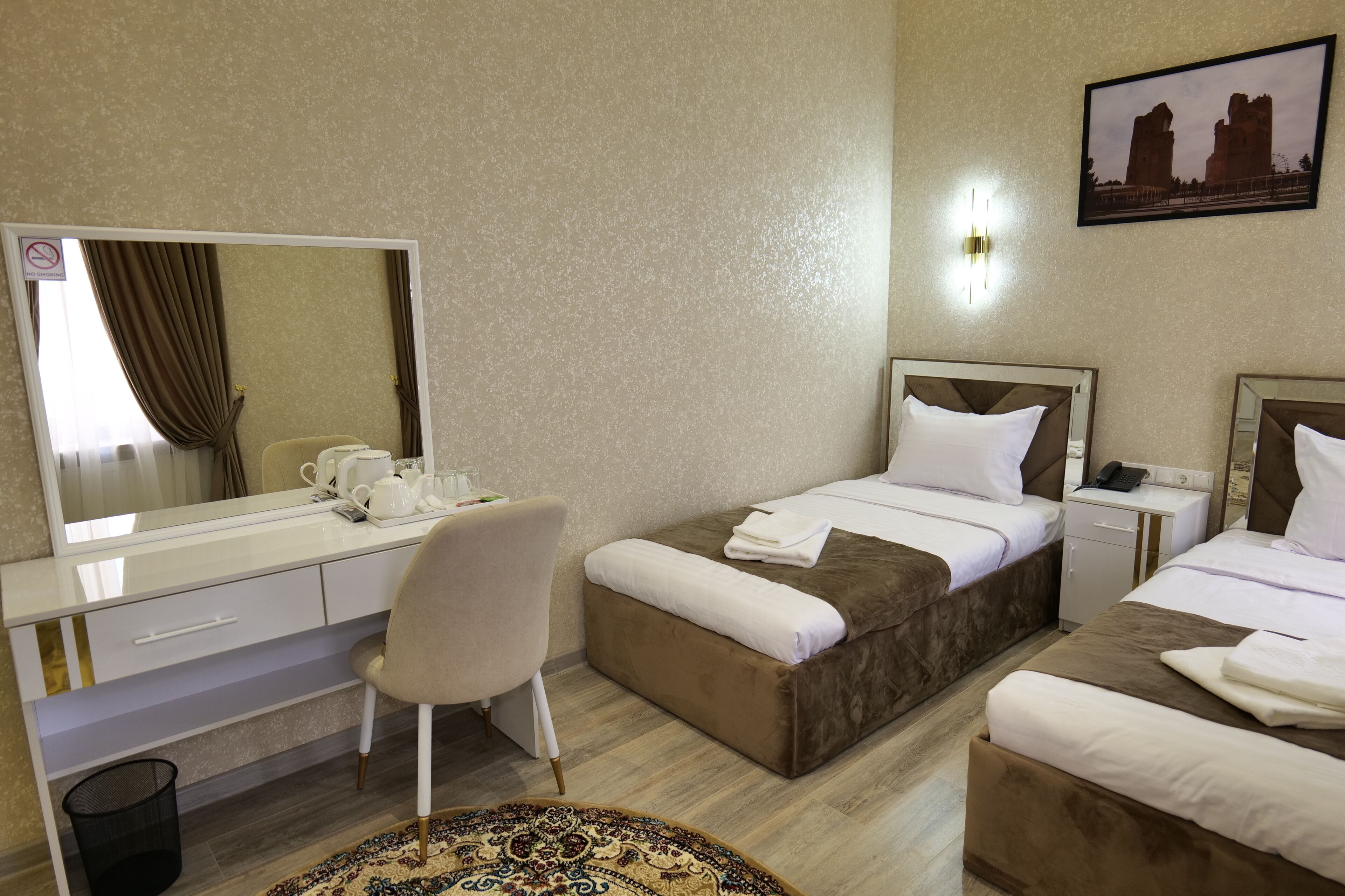 Habitación de hotel con dos camas, un escritorio y una silla, un espejo grande y una mesita de noche con un teléfono.