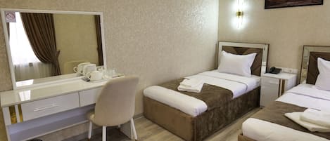 A hotel room with two beds, a desk with a chair, a large mirror, and a small bedside table with a phone.