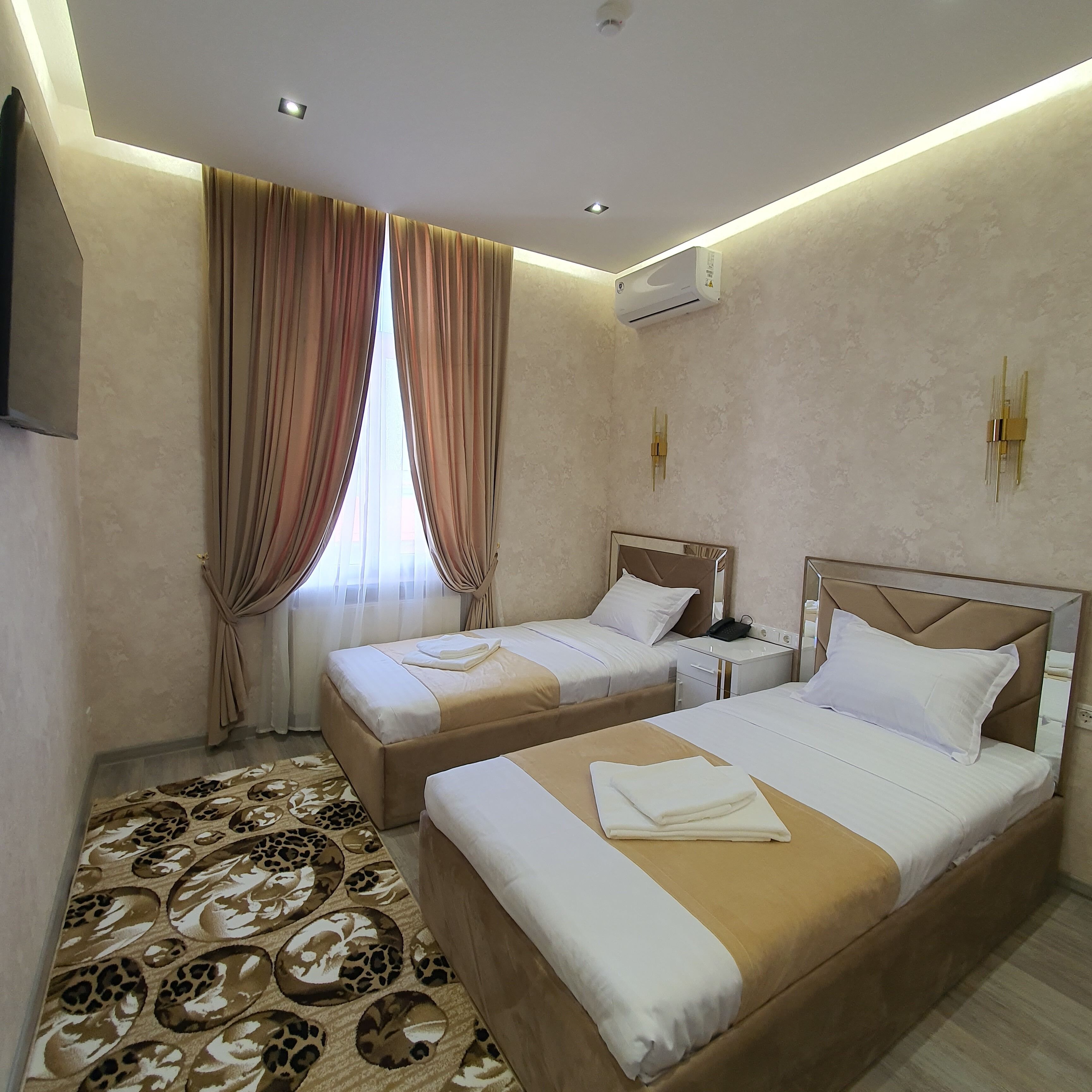 A hotel room with two beds, a patterned carpet, beige walls, and an air conditioning unit.