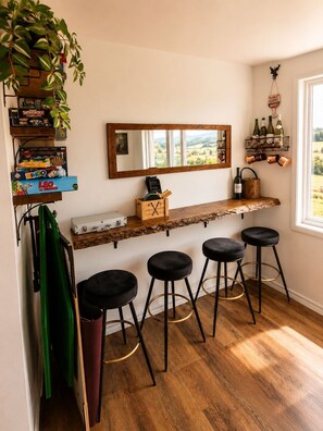 Un espace bar avec un comptoir en bois, trois tabourets noirs, un miroir et une vue sur la campagne.