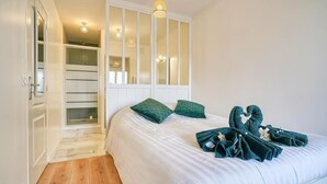 A bedroom with a bed, green pillows, and towels arranged on the bed. There is a closet with a mirror and a door leading to a hallway. - ''diamant'' (Choisy-le-Roi)